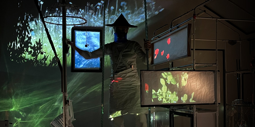 Photo du spectacle de la compagnie petites perceptions représentant une personne sur scène avec projections vidéo de nature et maison tubulaire